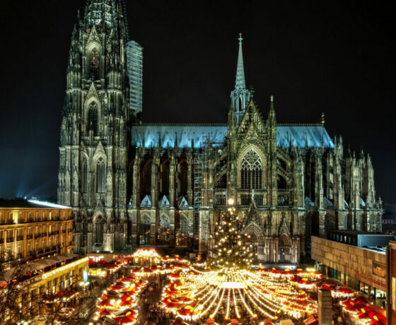 Beleuchteter Kölner Weihnachtsmarkt mit Dom im Hintergrund. Rechts ist das Römisch Germanische Museum und der Musical Dome zu sehen.