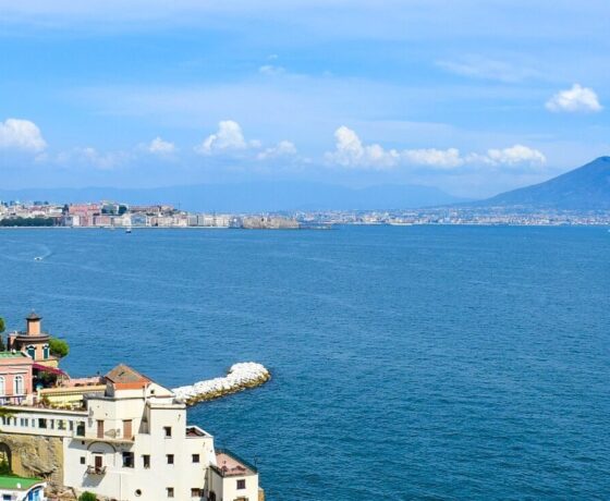 Blick auf eine malerische italienische Küstenstadt mit pastellfarbenen Häusern und einem klaren blauen Himmel über dem Meer.