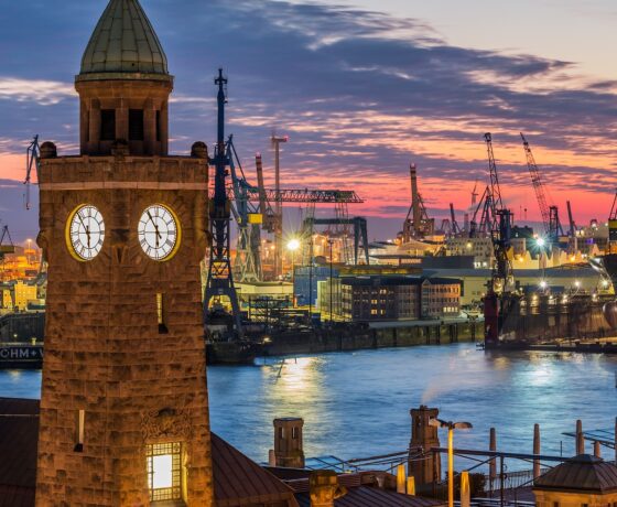 Das Bild zeigt den Hamburger Hafen mit Blick auf die Elbphilharmonie. Kräne, Schiffe und moderne Architektur prägen das Stadtbild.