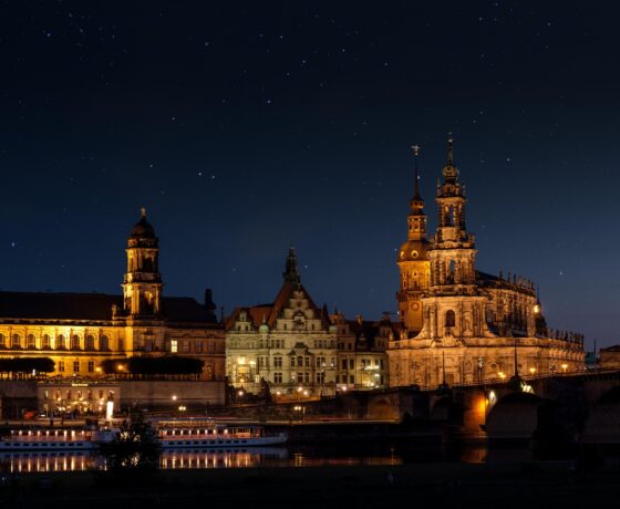 Das Bild zeigt die festlich beleuchtete Dresdner Altstadt im Advent – mit Hofkirche, Residenzschloss und stimmungsvoller Spiegelung in der Elbe bei Nacht.