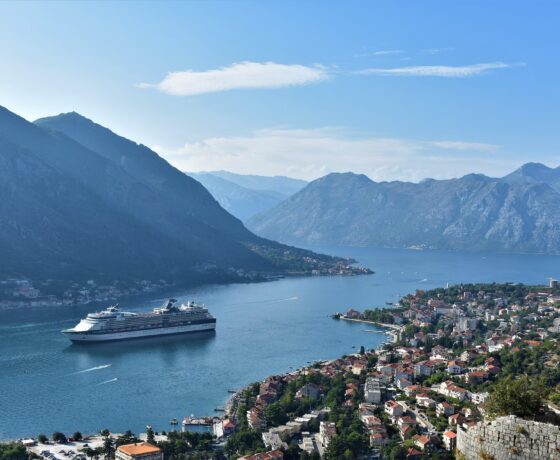 Das Bild zeigt die Bucht von Kotor in Montenegro mit einem Kreuzfahrtschiff, umgeben von Bergen und einer malerischen Küstenstadt.