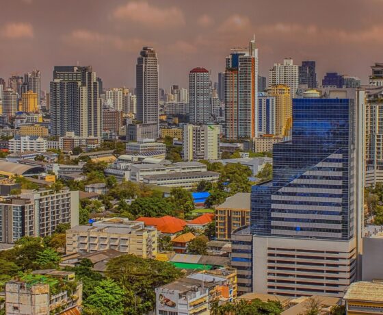 Moderne Stadtansicht von Bangkok mit vielen Hochhäusern, grünen Bäumen und einem bewölkten Himmel.
