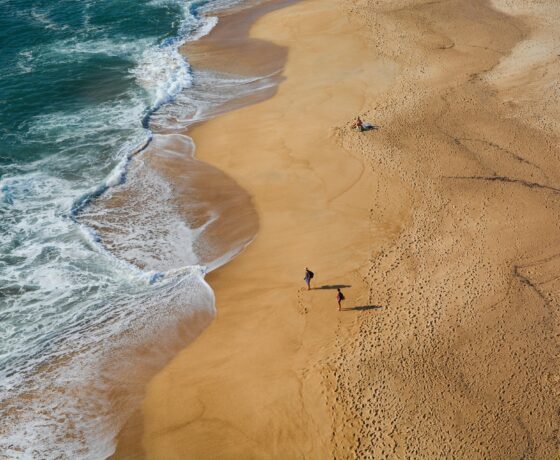 Weitläufiger Sandstrand in Portugal mit sanften Wellen, Fußspuren im Sand und wenigen Spaziergängern.