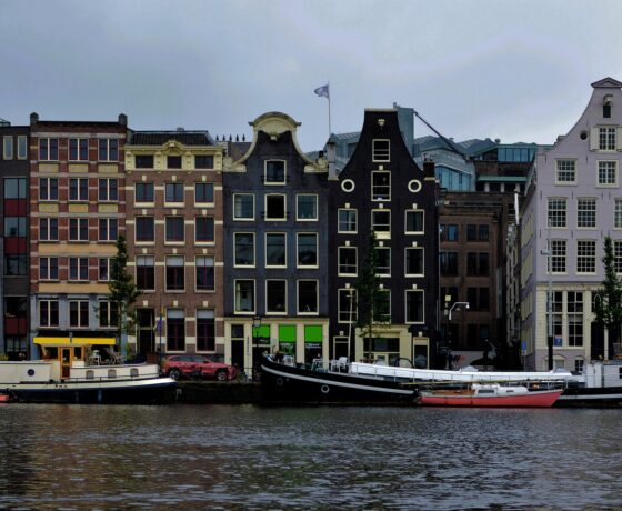 Typische Amsterdamer Grachtenansicht mit schmalen Giebelhäusern und Hausbooten am Wasser.