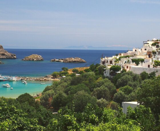 Blick auf Rhodos: Weiße Häuser am Hang, grünes Umland und türkises Meer mit Booten.