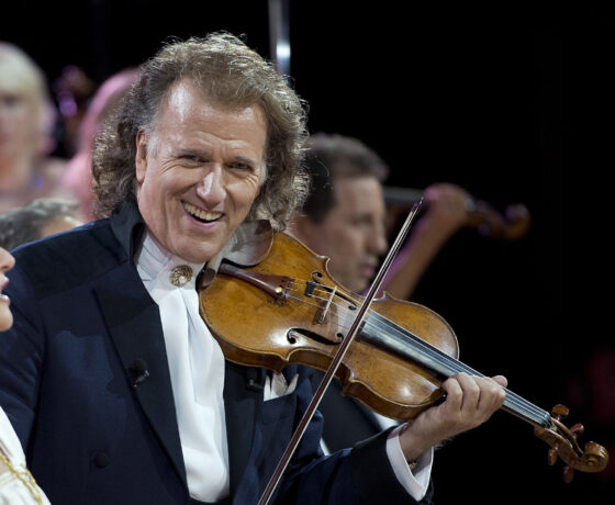 André Rieu spielt lächelnd Geige auf einer Bühne.
