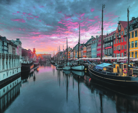 Abendstimmung im Hafen von Kopenhagen mit bunten Häuserfassaden, Segelbooten und dramatischem Himmel bei Sonnenuntergang.