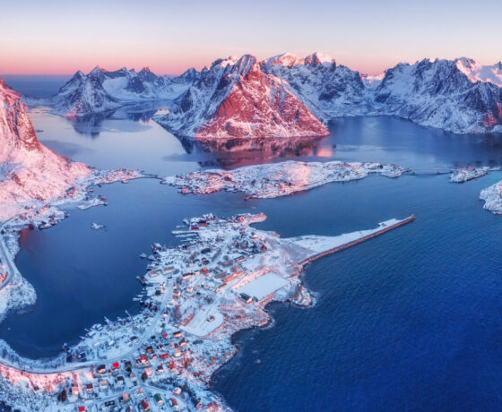 Verschneite Winterlandschaft in Norwegen mit Inseln und Bergen im Sonnenuntergang.