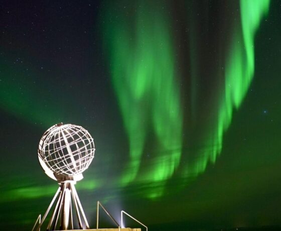 Grün leuchtende Polarlichter bei Nacht mit dem beleuchteten Globus am Nordkap.
