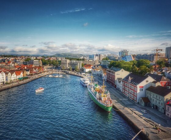 Das Bild zeigt einen Hafen mit einem festgemachten Schiff, umgeben von bunten Häusern und moderner Stadtarchitektur bei klarem, sonnigem Wetter.